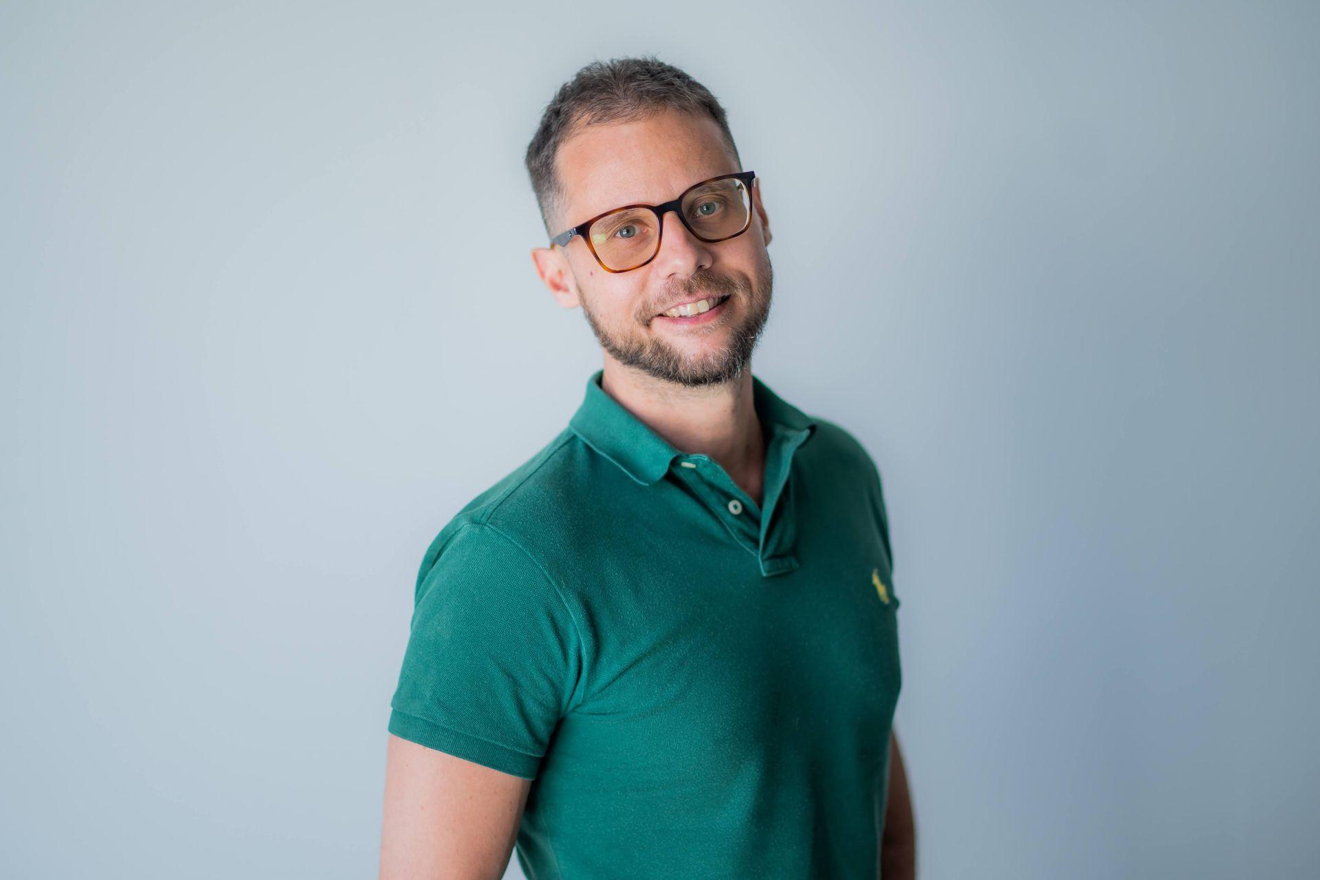 Alex Dogliotti, smiling and wearing a green polo shirt, standing against a plain light background.